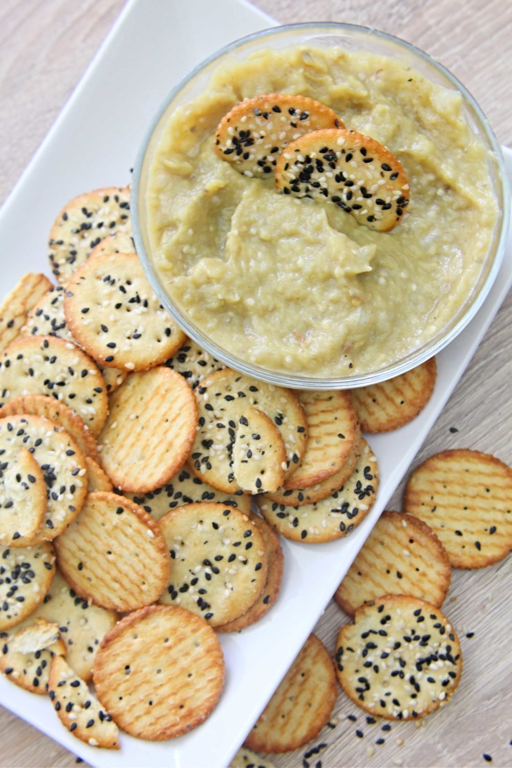 Roasted eggplant dip on a white serving plate with mixed seed crackers