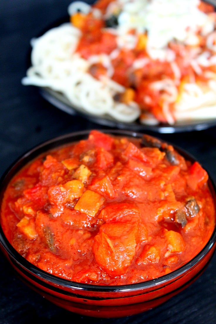 Vegetable Spaghetti Sauce in a bowl on black counter, next to a spaghetti dish