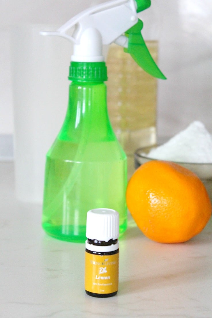 Image of homemade natural disinfectant for home in a green spray bottle, next to a bottle of essential oils and lemon fruit