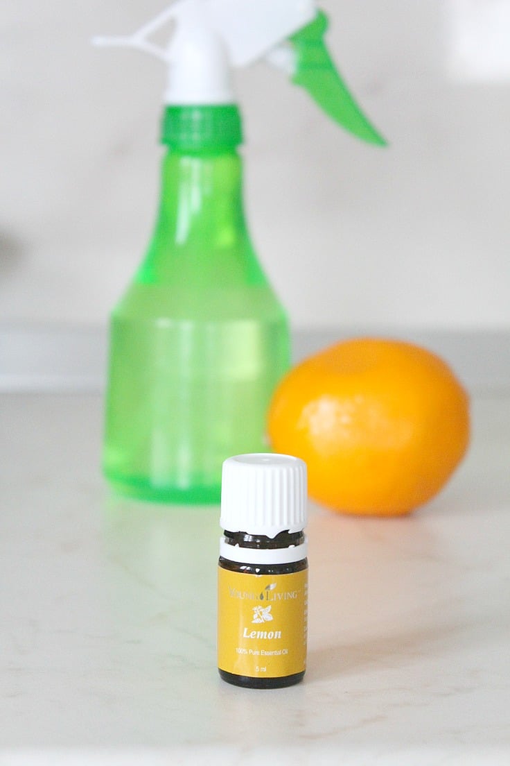 Image of lemon disinfectant in a light green spray bottle, next to a bottle of essential oils and a lemon fruit