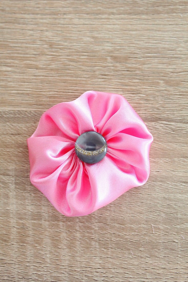 Fabric Yo Yo in pink satin, with gray button in the center, on oak table