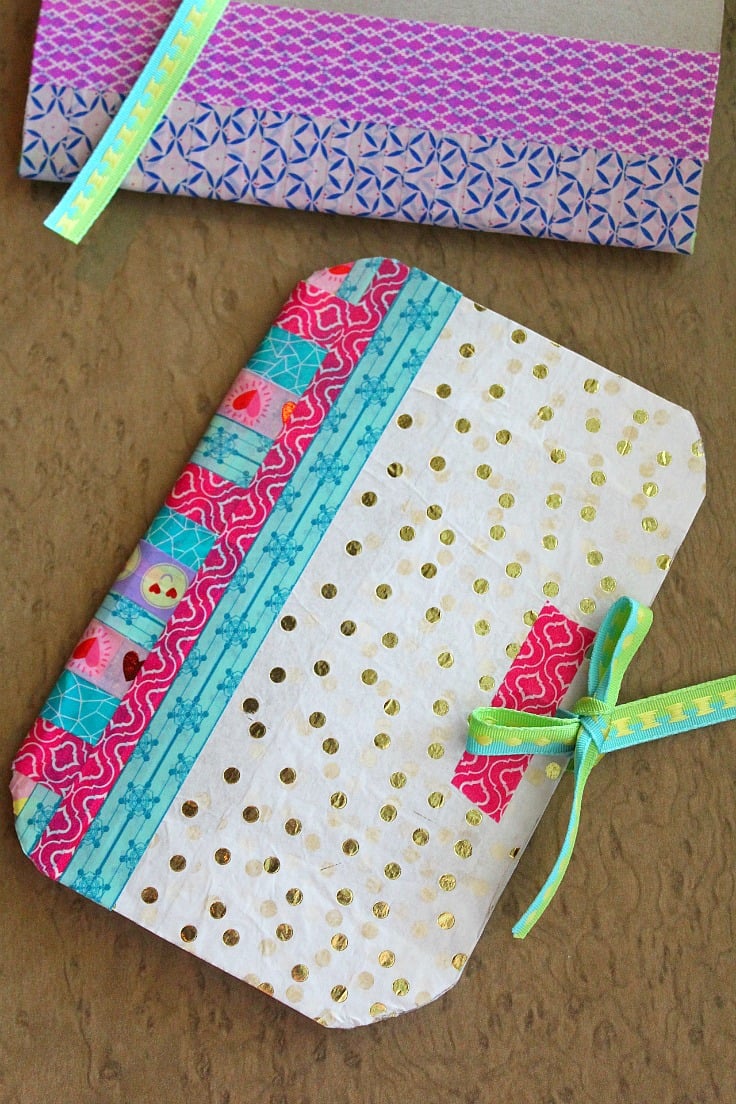 DIY notebook made with cereal box, tissue paper in gold polka dots, washi tape in various colors and ribbon