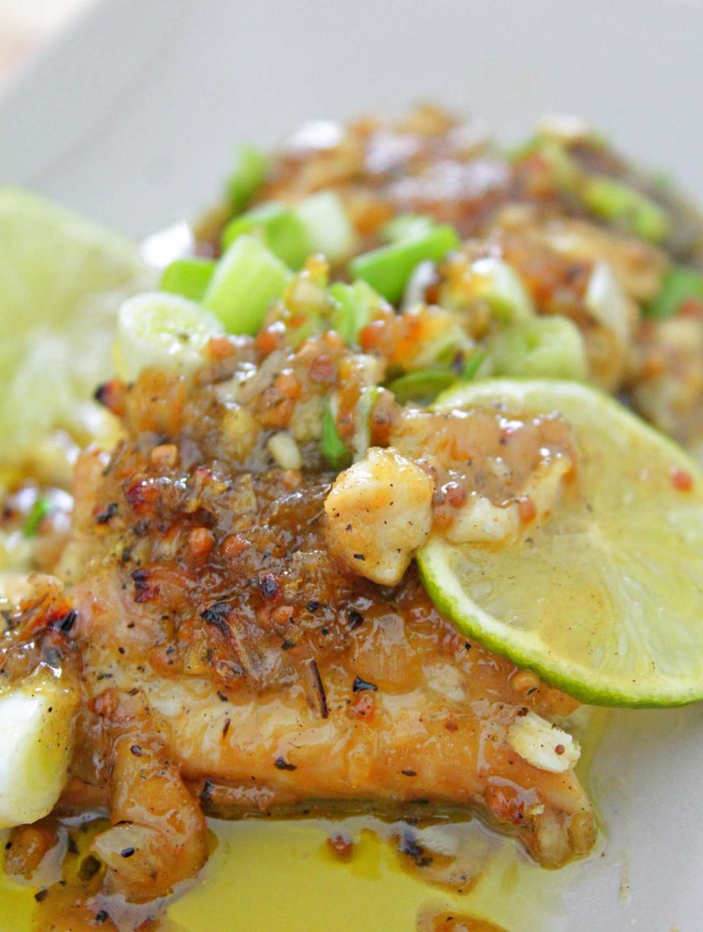 Baked fish in honey mustard sauce for fish sprinkled with green onions and served o a white plate with slices of lime