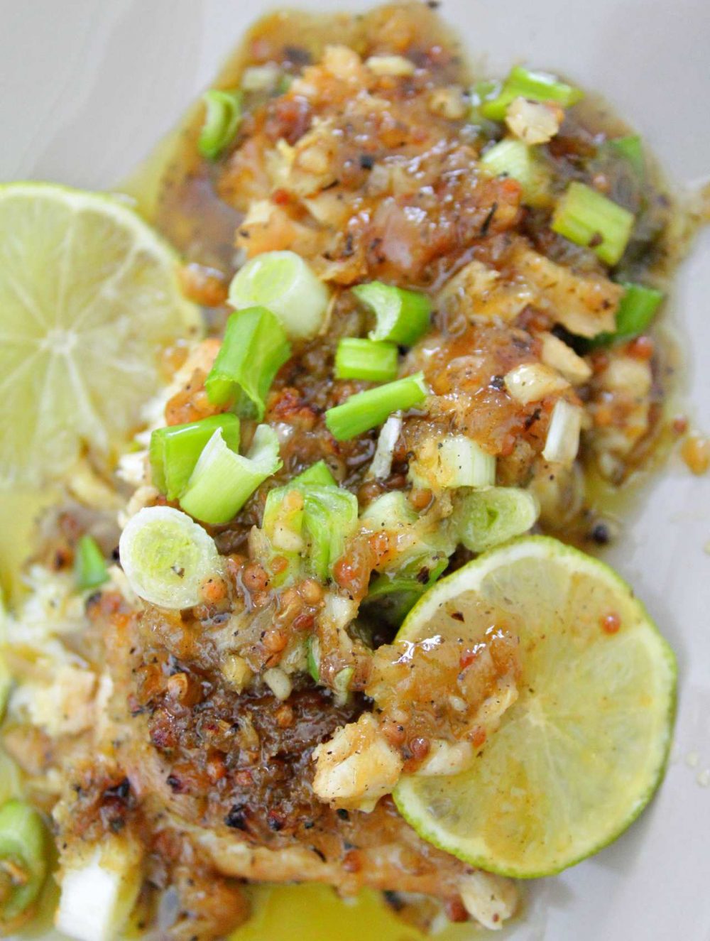 Marinated fish on a white serving plate, with chopped green onion and slices of lime