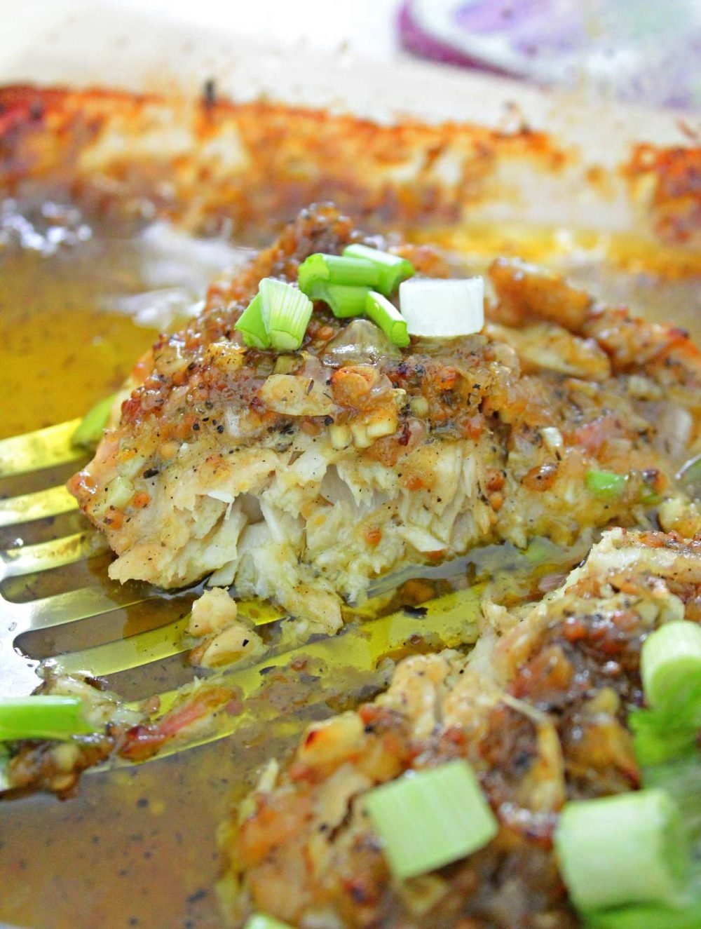 Fish with mustard sauce in a baking dish, on a turner, sprinkled with green onions