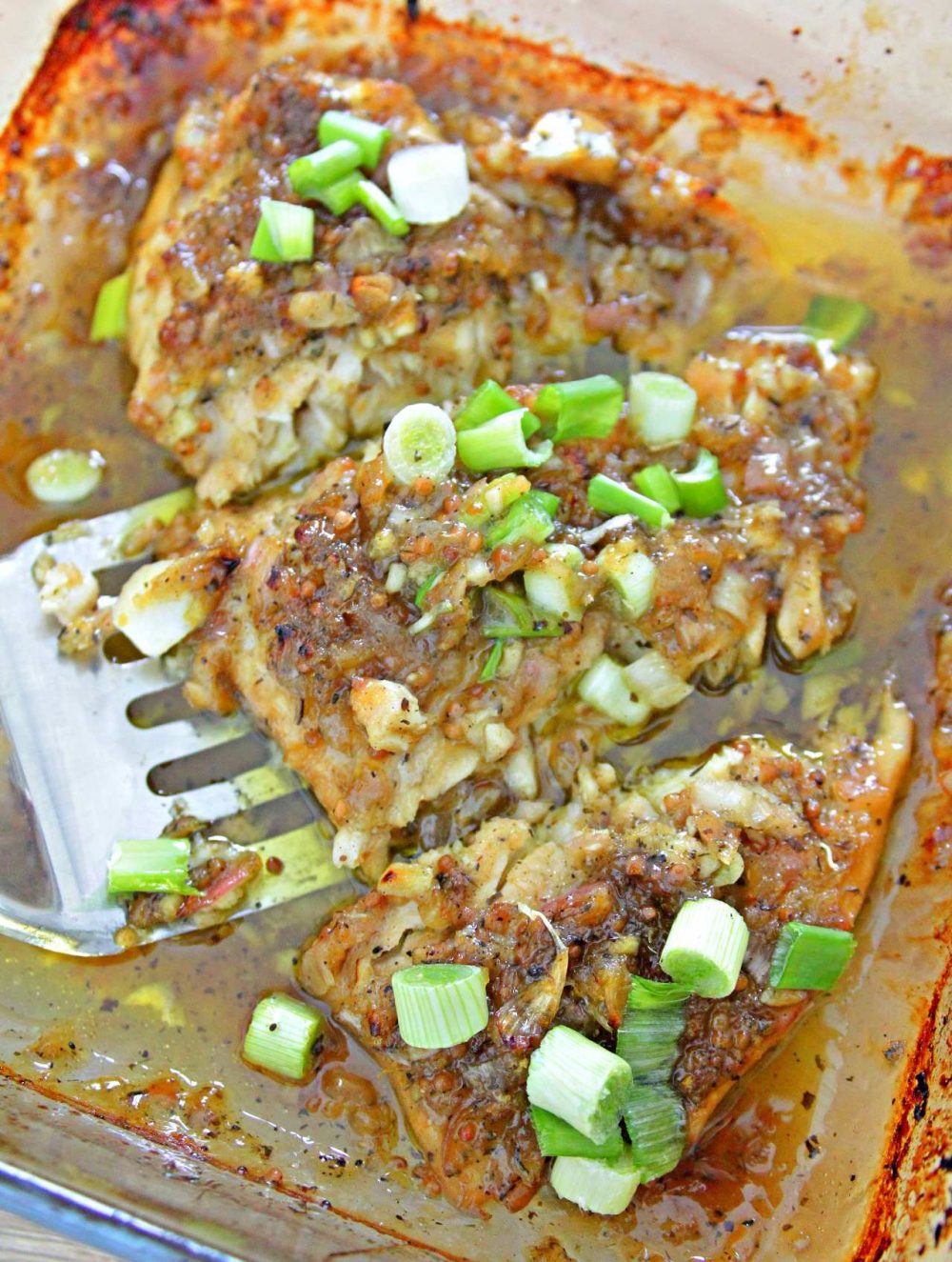 Baked fish on a turner in a baking dish, covered in honey mustard sauce for fish and sprinkled with chopped green onions