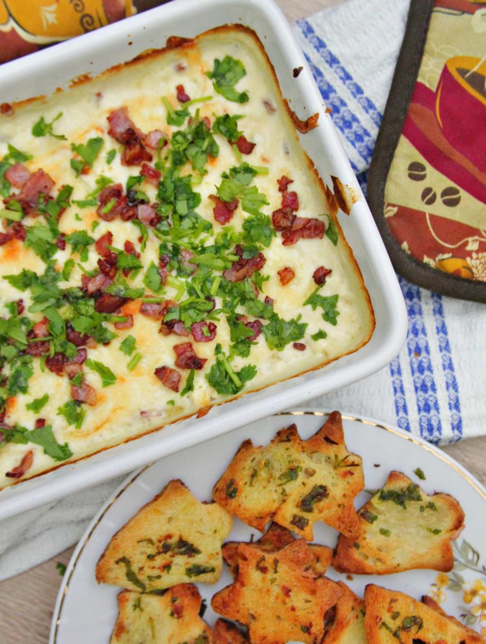 Bread chips next to a casserole of hot cheese dip with bacon and parsley