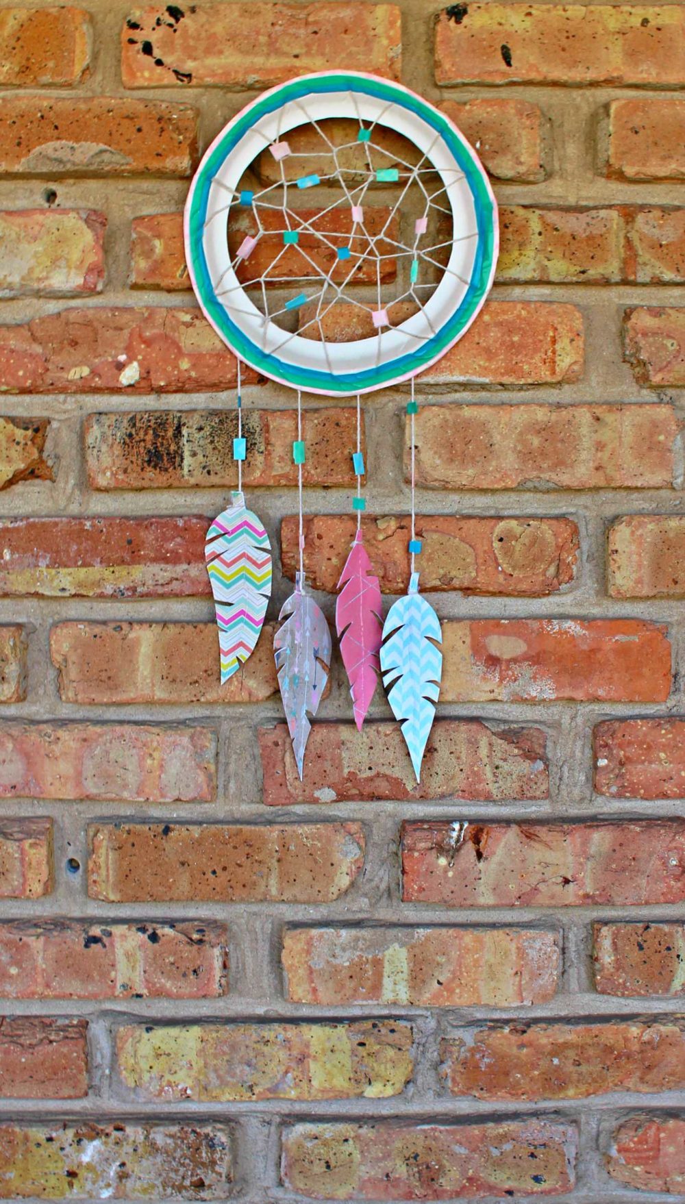 Paper dream catcher made with paper feathers, twine and washi tape and displayed on a wall