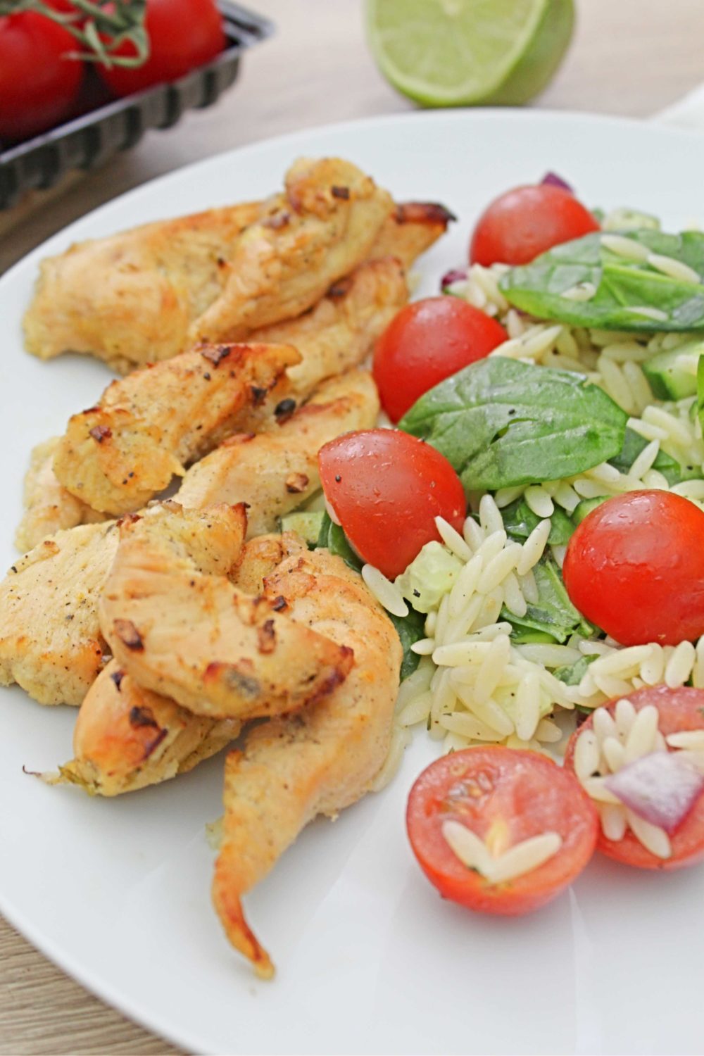 Lemon chicken orzo with a baby spinach and cherry tomatoes salad, on a white plate