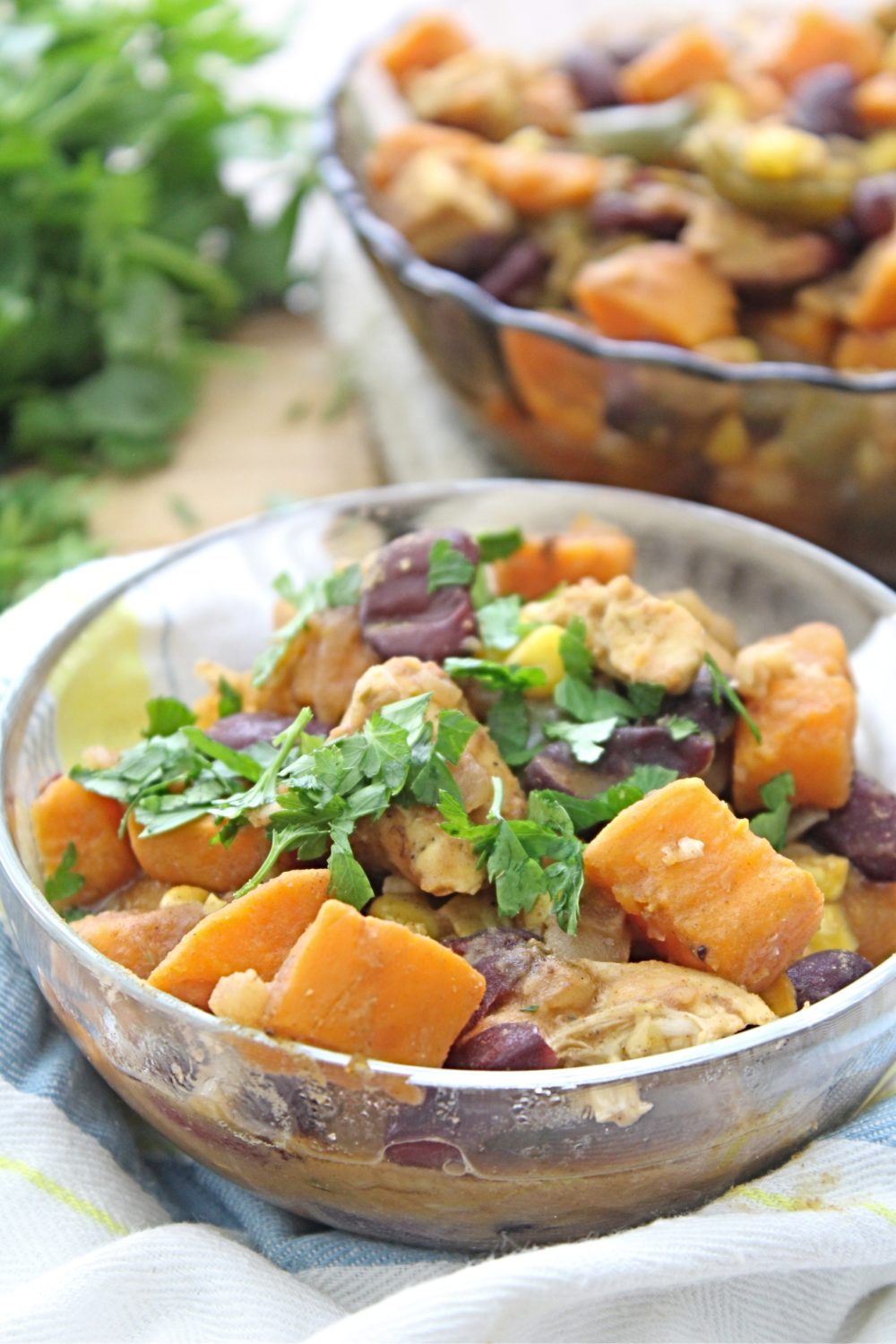 Transparent bowl of Healthy chicken chili with sweet potatoes sprinkled with fresh parsley