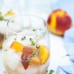 Peach gin cocktail in a glass dressed with peach wedges and thyme sprigs