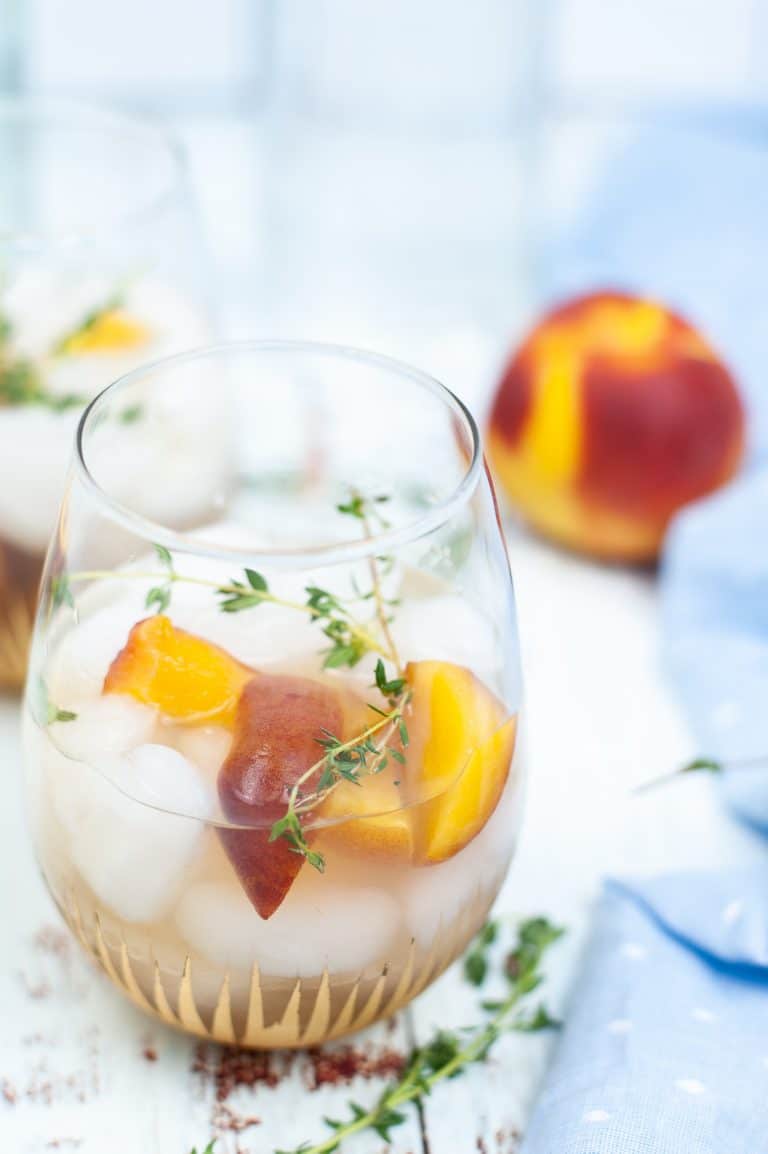 Peach gin cocktail in a glass dressed with peach wedges and thyme sprigs