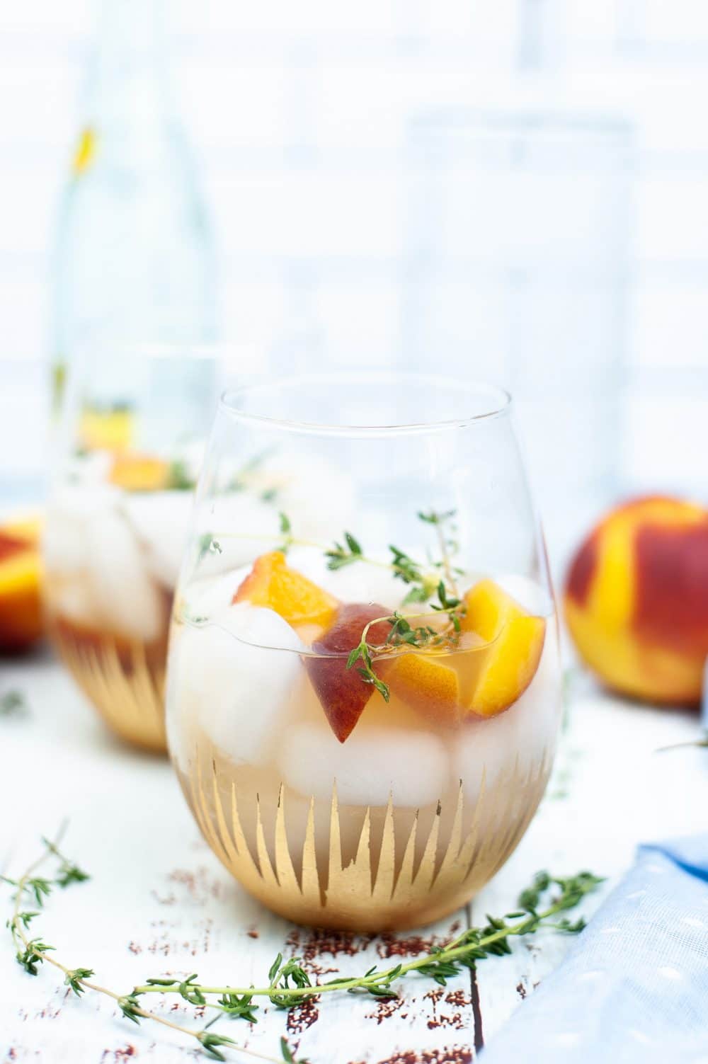 Peach syrup cocktail in a glass dressed with slices of peaches and thyme sprigs