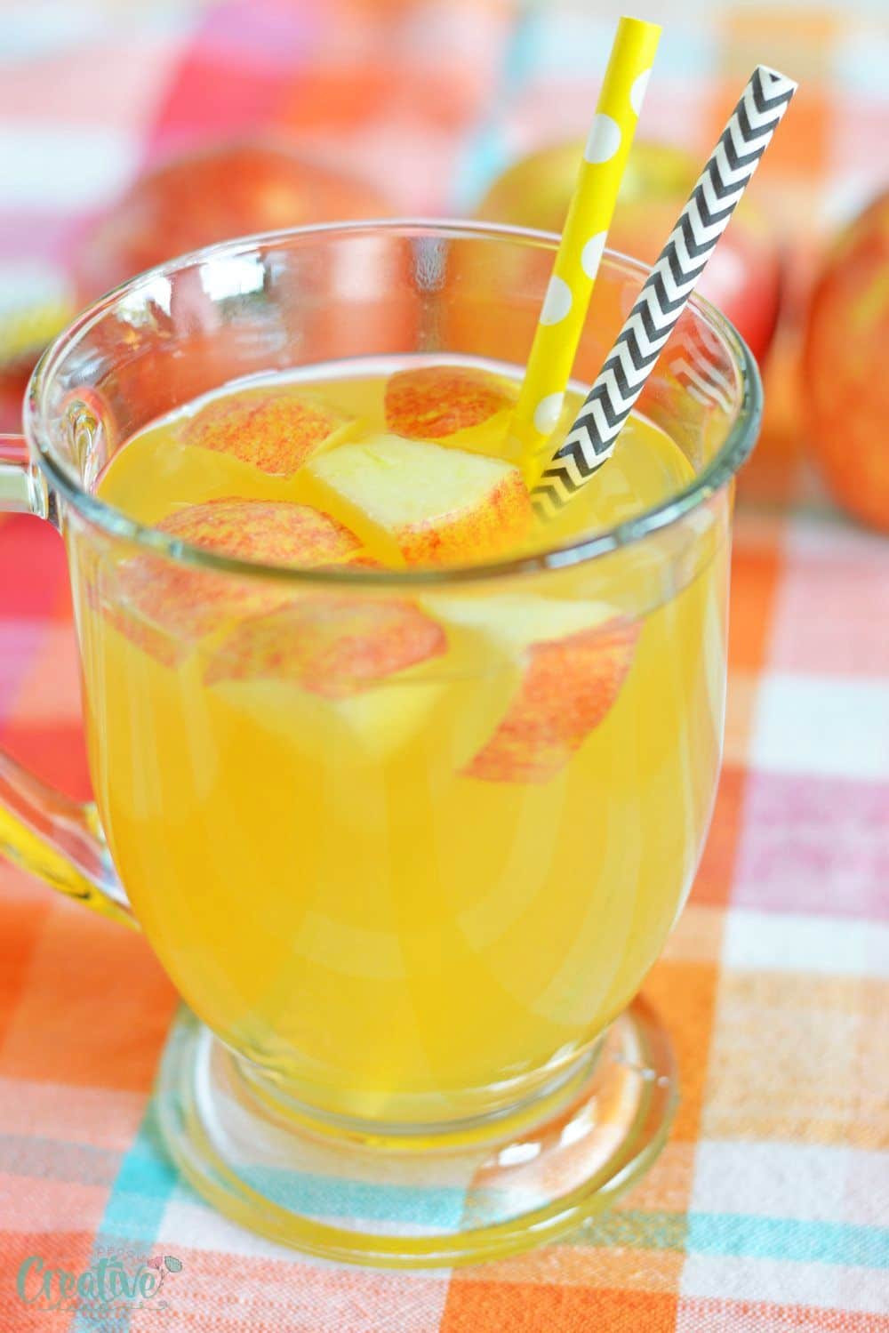 Image of alcoholic apple cider in a mug, decorated with apples and paper straws