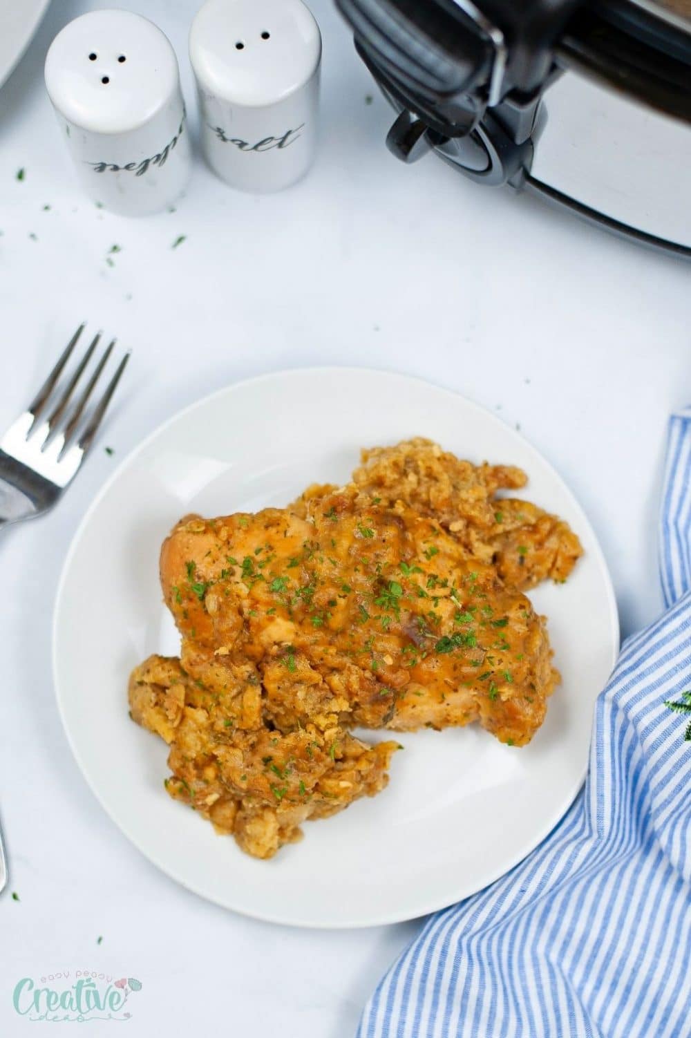 Image of chicken stuffing casserole on a white plate next to the slow cooker where it was cooked