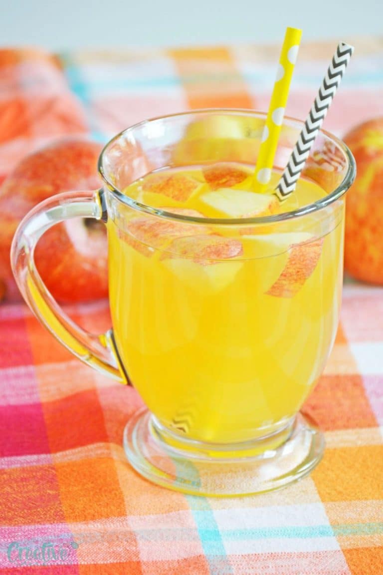 Spiked apple cider in a mug, decorated with apples and paper straws