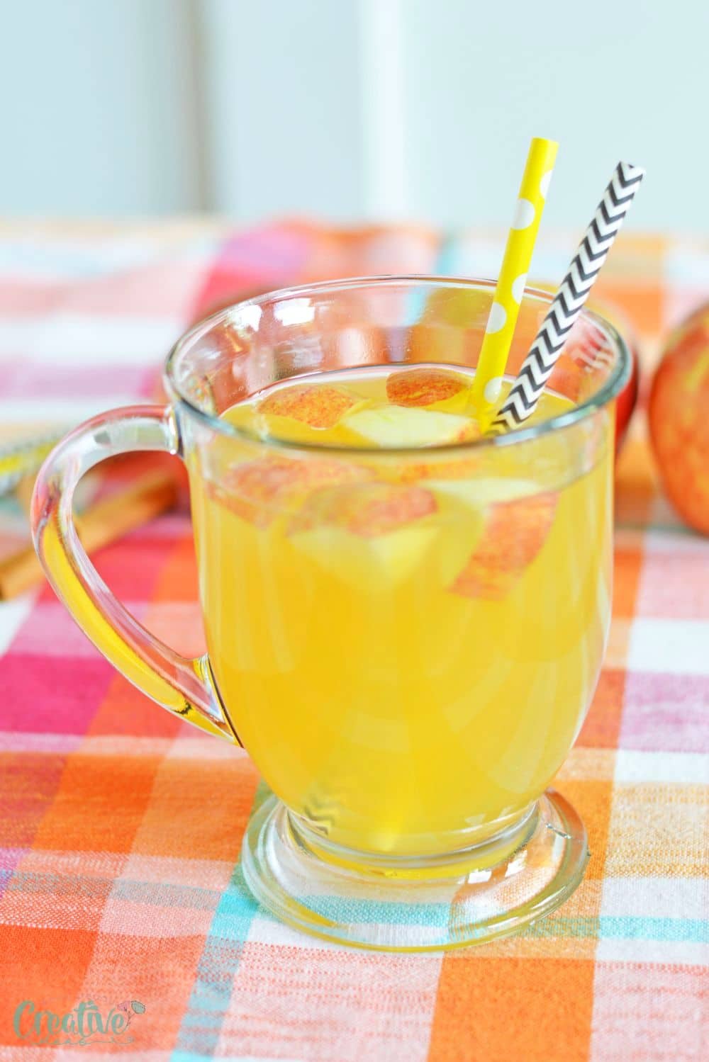 Close up image of spiked caramel apple cider in a drinking mug, decorated with apples and paper straws