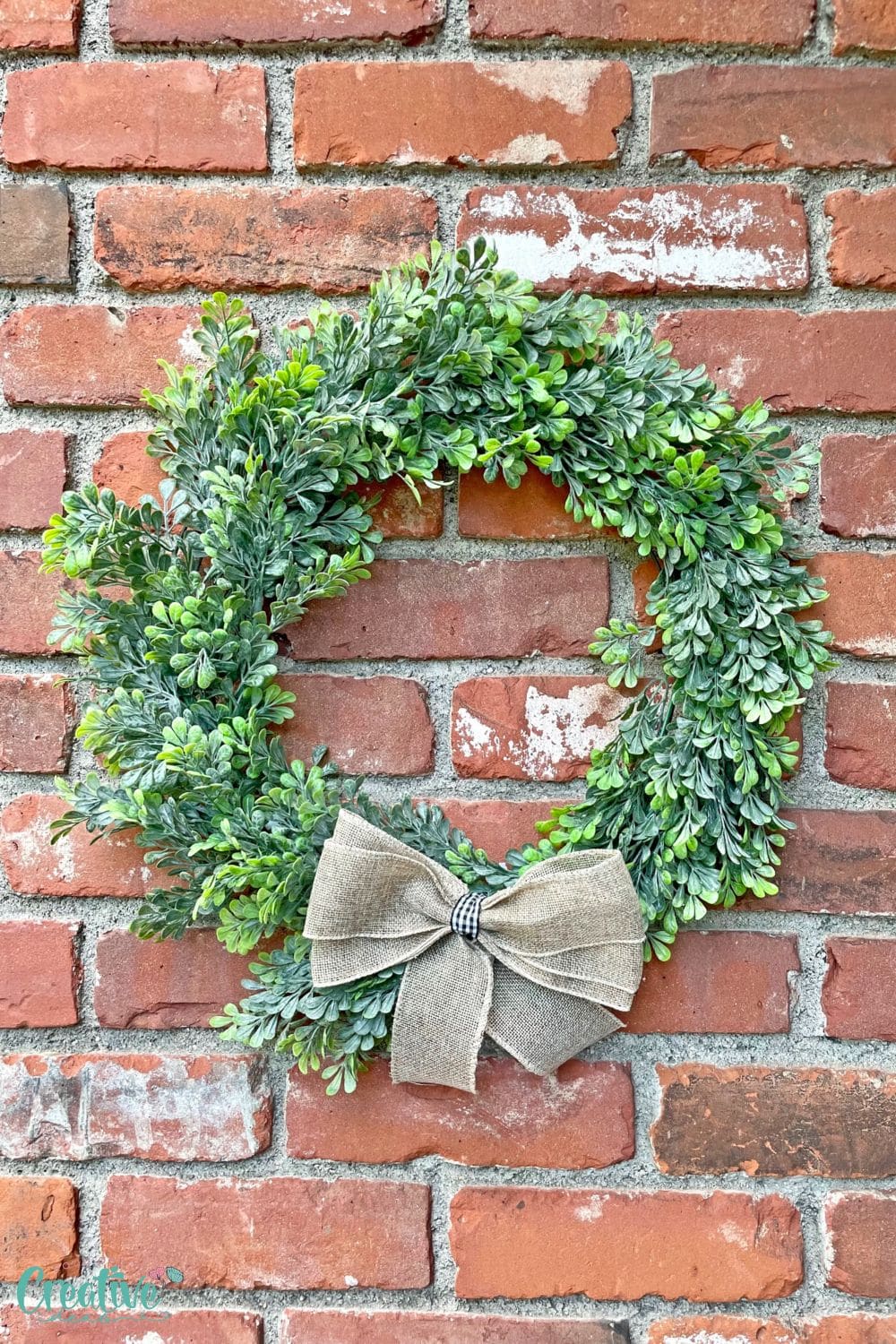 Close up image of farmhouse Christmas wreath made with fake boxwood and a bow