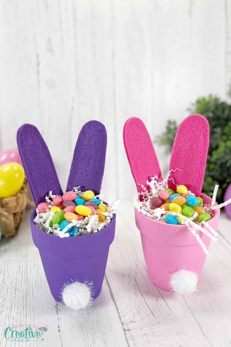 Two small clay pots filled with colorful candy and candy eggs, and decorated with pompoms to resemble bunny butts, perfect for a sweet treat or festive celebration.