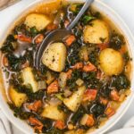 A bowl of chorizo and kale soup with potatoes, chorizo, and kale, served hot and garnished with fresh herbs.