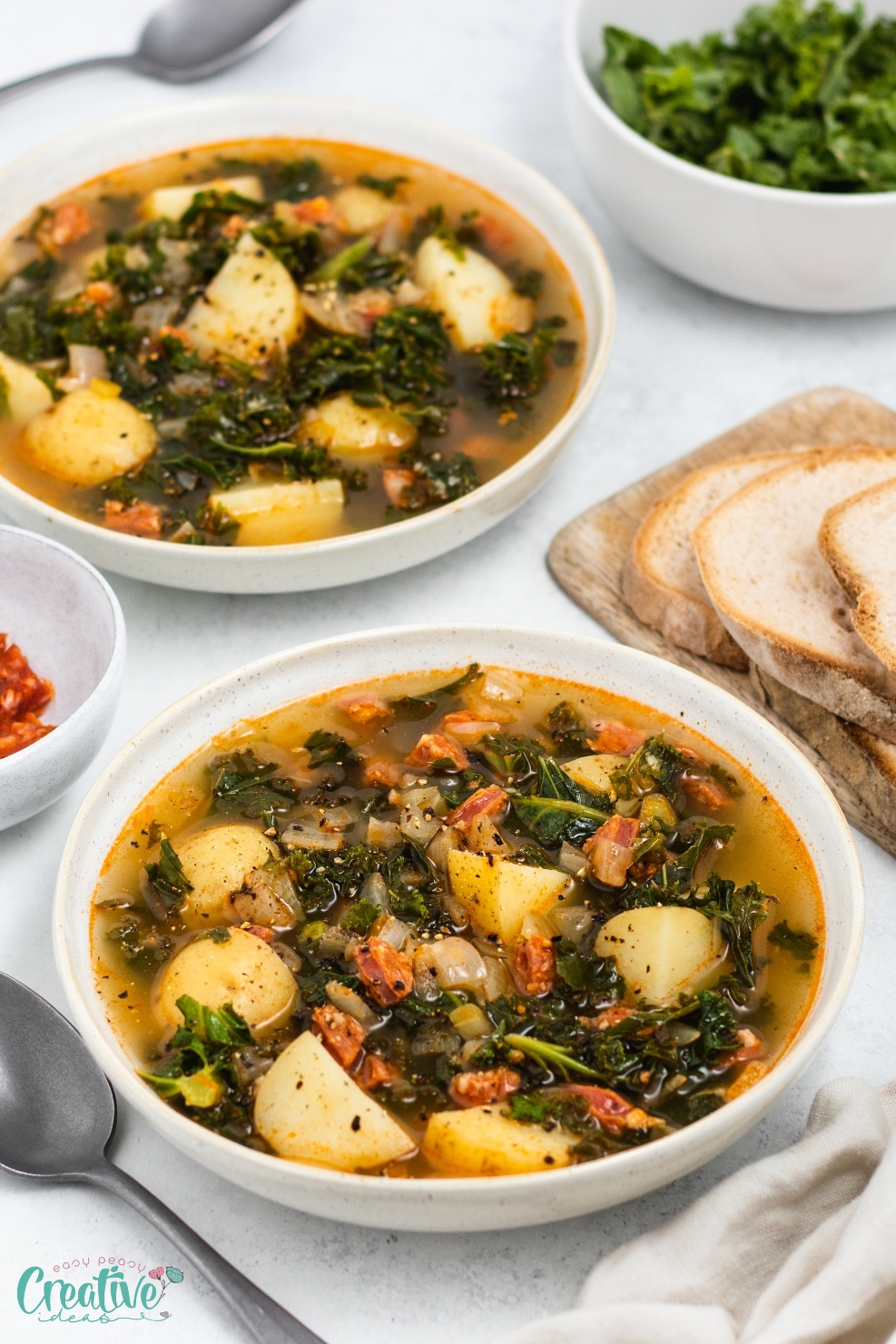 Two bowls of kale soup with chorizo featuring chunks of potatoes and fresh kale leaves, served piping hot.