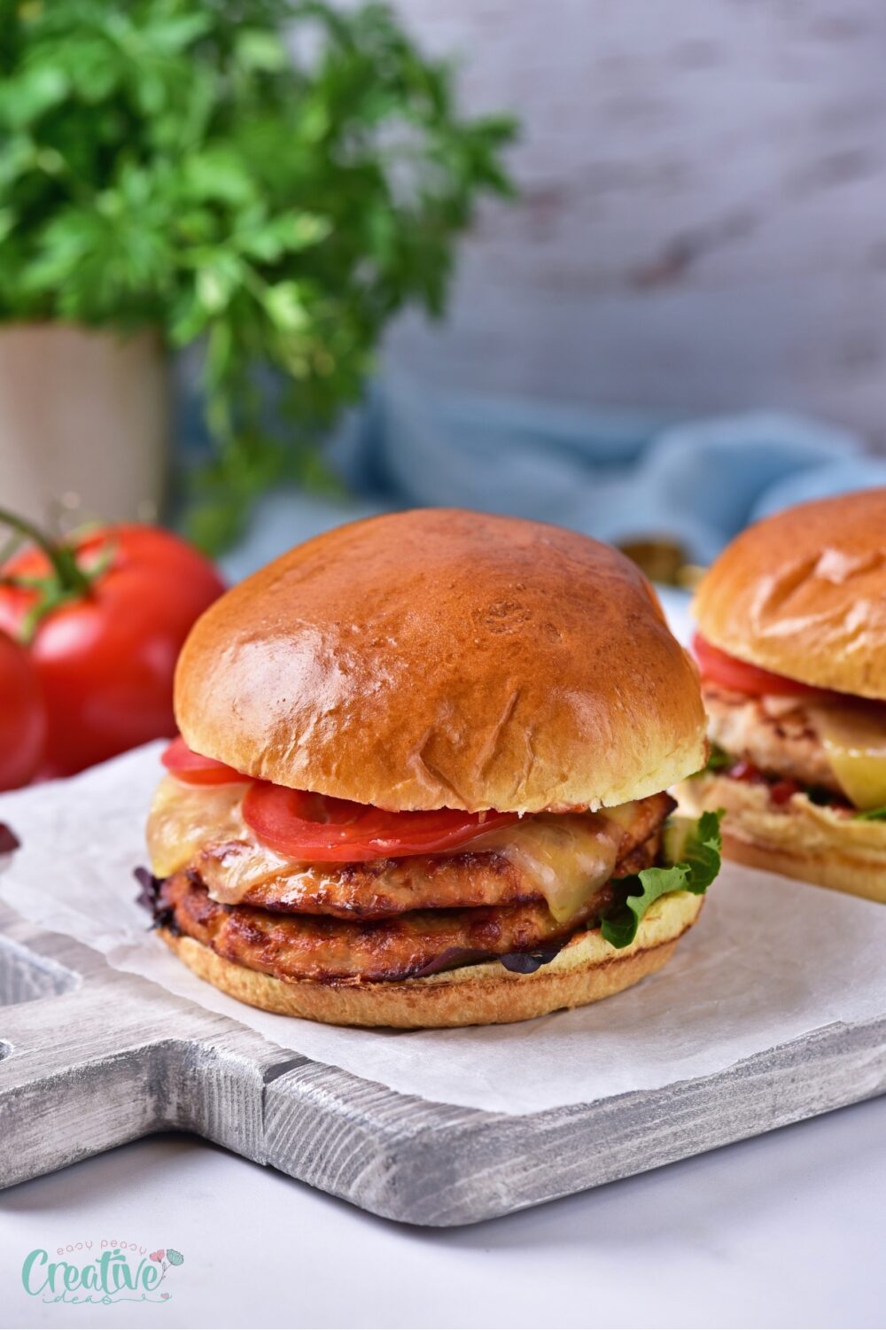 Two ground turkey burgers topped with fresh tomatoes and lettuce, resting on a wooden cutting board.