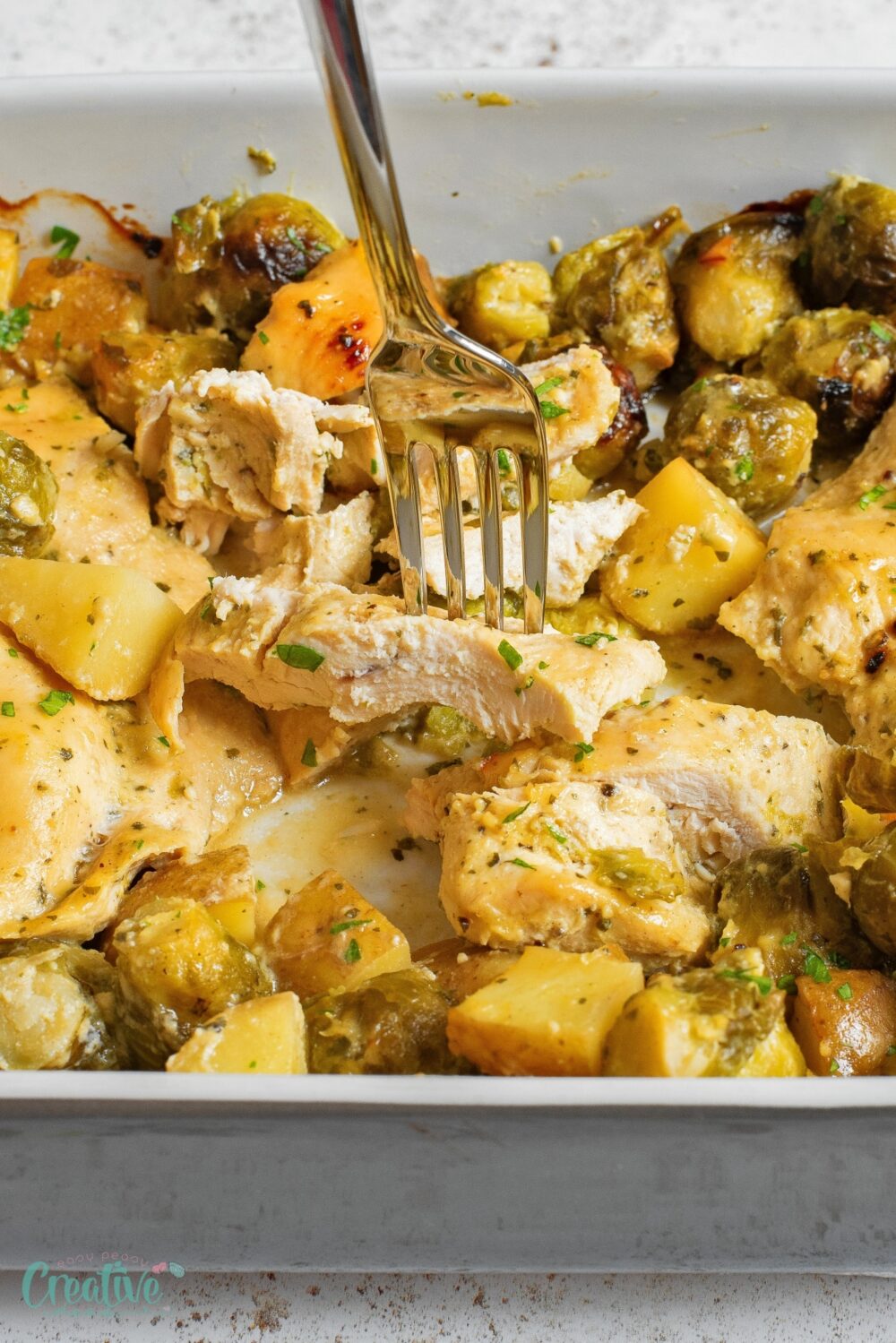 Baked honey Dijon chicken breast with vibrant Brussels sprouts and golden potatoes, all in a warm baking dish.