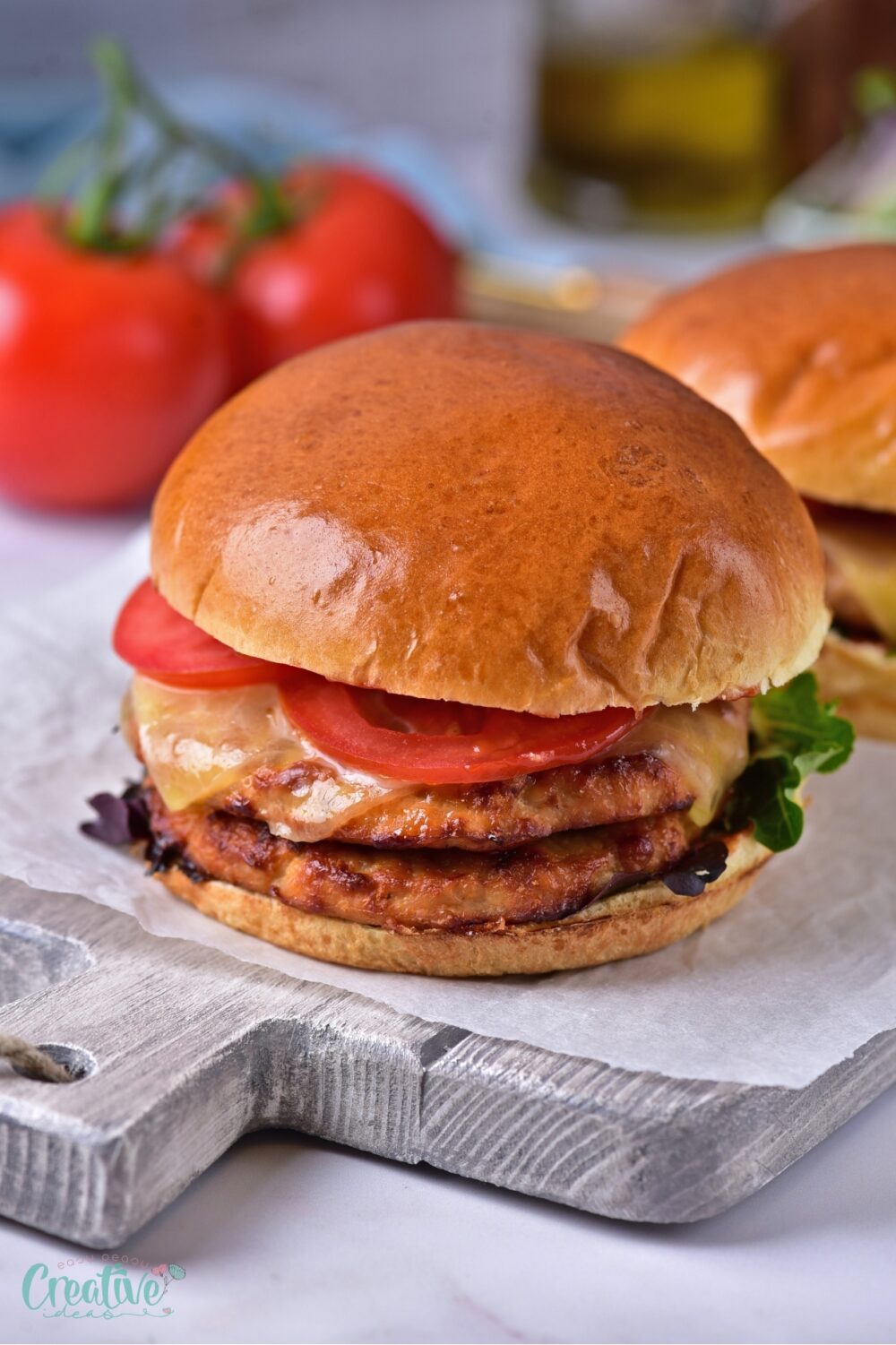 A cutting board displays two delicious oven turkey burgers, garnished with vibrant tomatoes and crisp lettuce.