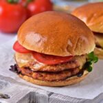 A cutting board displays two delicious oven turkey burgers, garnished with vibrant tomatoes and crisp lettuce.